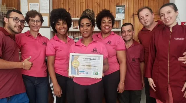 Oito pessoas da equipe da Galera Animal, de camisa polo rosa e vinho, atrás do balcão da loja, segurando um certificado